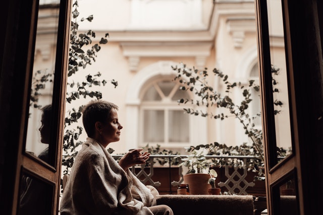 žena sedí na balkóne a všímavo pije kávu